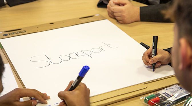 Hands writing on a piece of paper with the word Stockport in the centre