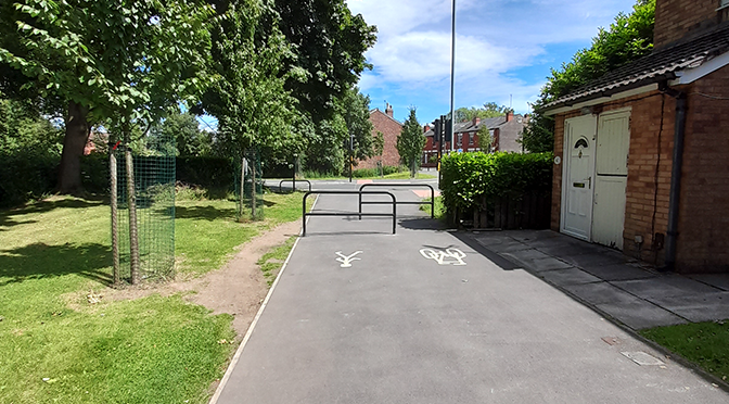 An informal footpath on the grass around a safety barrier at the end of a cycle lane and footpath.