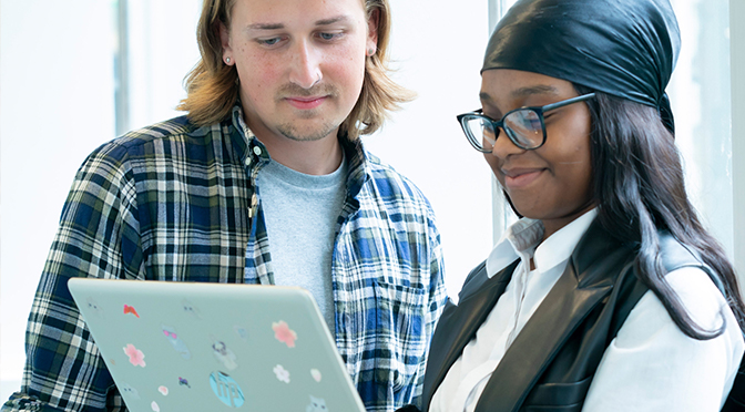 Two young people look at a laptop