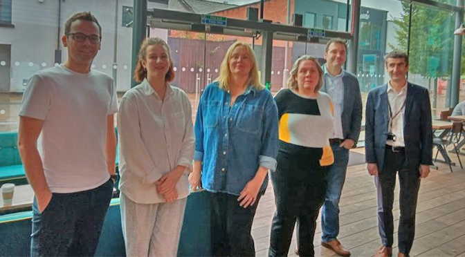 Six presenters, 3 men, 3 women, standing in a cinema foyer