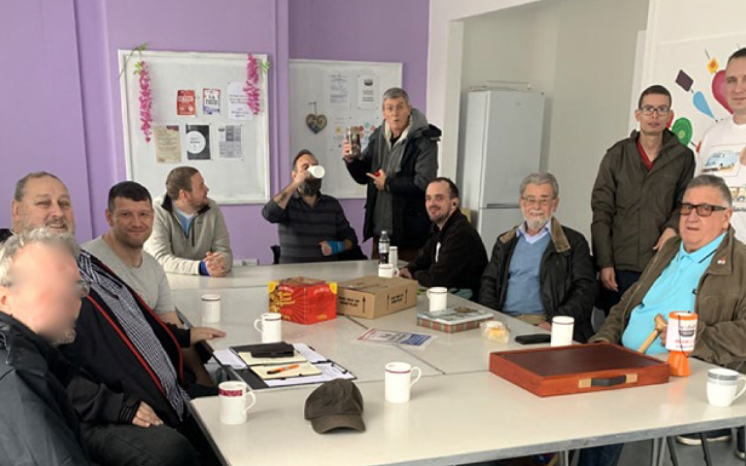 A group of men of all ages around a table with a mug each.