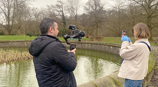 A person filming another person looking at their mobile phone in a park